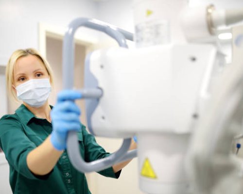 Female technician adjusts X-Ray machine. Female radiologist is going to take an Xray of patient in X-ray room of modern clinic. Medical examination of people